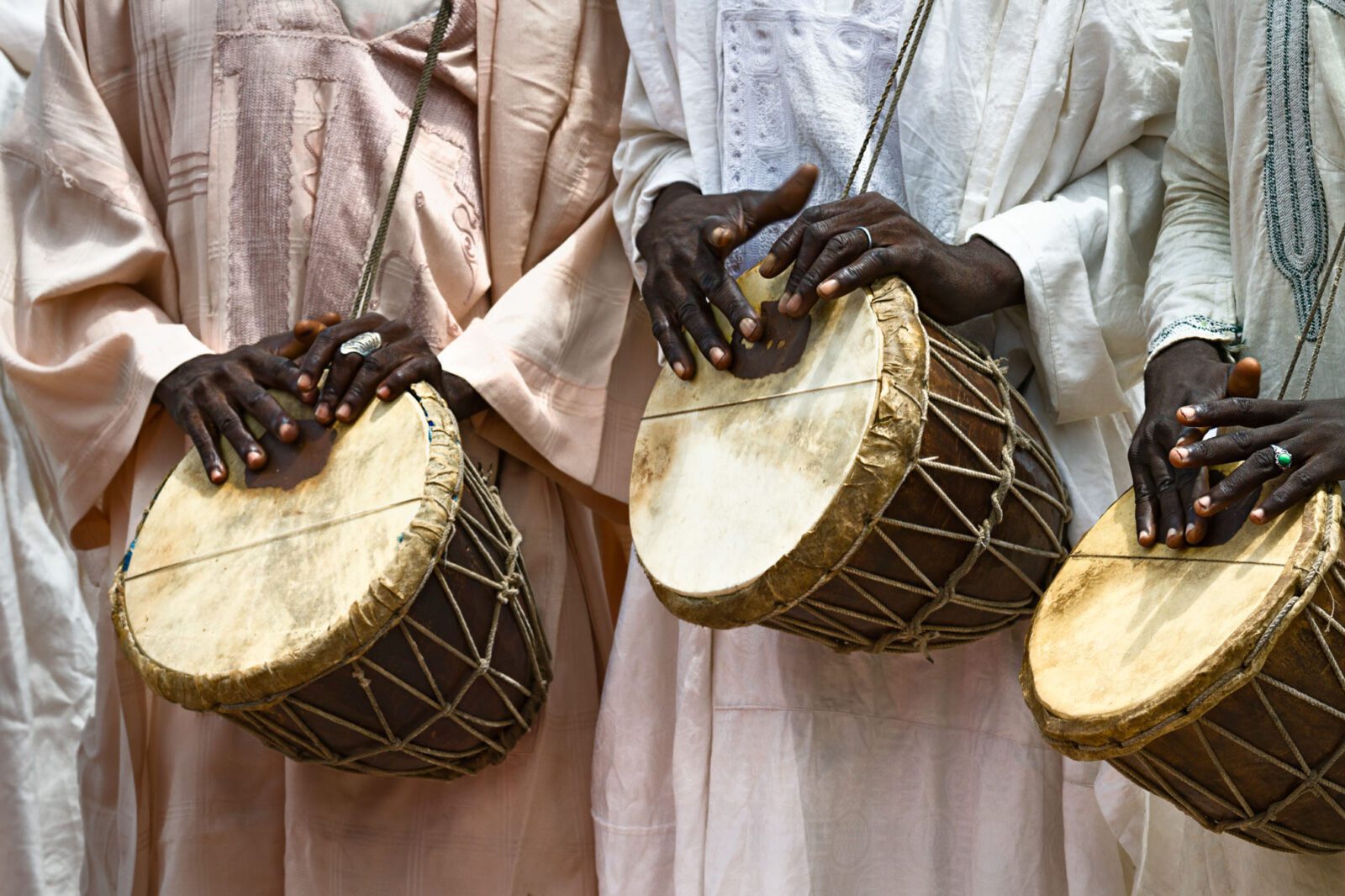 Photo of three drummers wearing traditional clothes, playing traditional drums, heads not visible