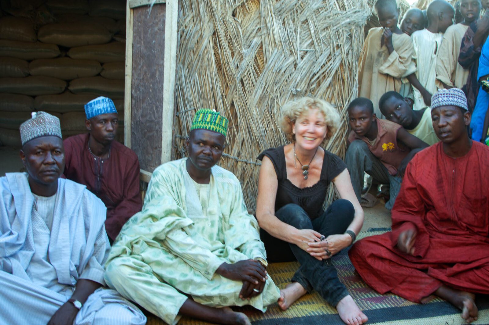 Sitting among traders and children on a woven mat outside a grass-built warehouse at Gashua Potash Market, Yobe State, Nigeria.