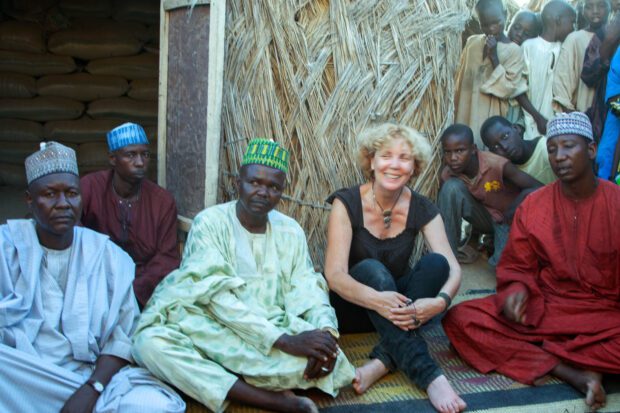 Sitting among traders and children on a woven mat outside a grass-built warehouse at Gashua Potash Market, Yobe State, Nigeria.