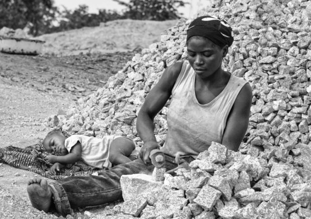 Mother Breaking Stones with Sleeping Baby | Gudi, Nasarawa | Irene Becker Photography | Irene Becker Photography A mother breaks stones for construction in Gudi, Nasarawa State, Nigeria, while her baby sleeps beside her amid dust and heat.