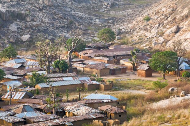 Dawn view of Turunku village, Kaduna State, with mud houses, tin roofs, rocky mountains, and baobab trees.