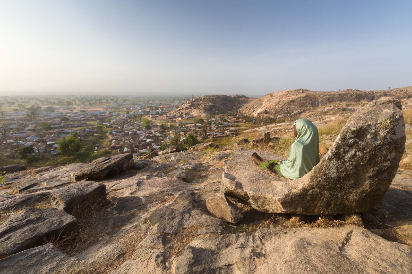 Mundeya sitting in Queen Amina’s Stone Seat at sunrise, overlooking Turunku village, Kaduna State.