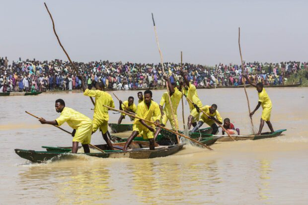 Two Boys Canoe Race, Matan Fada River, Argungu | Irene Becker Photography | Irene Becker Photography Argungu Fishing Festival Two boys compete in a canoe race on the Matan Fada River during Argungu’s youth water sports day, showcasing skill and determination.